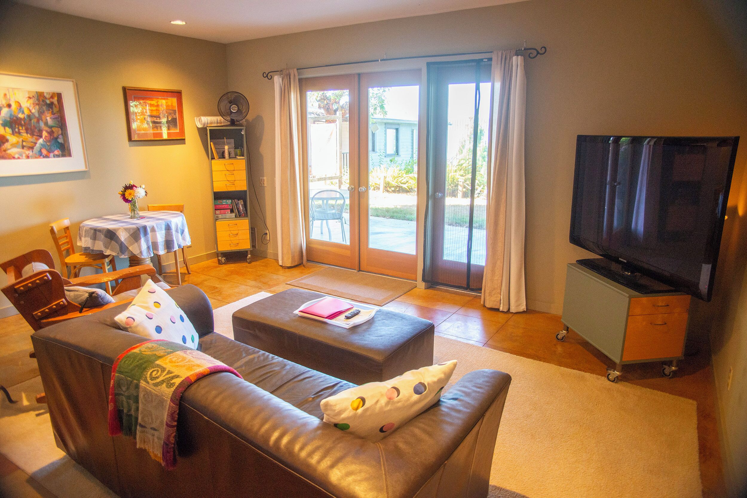 A living room with a sofa, ottoman, television, and a dining area with a table and chairs.
