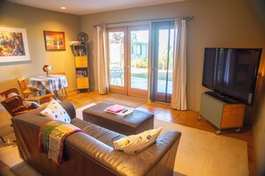 A living room with a sofa, ottoman, television, and a dining area with a table and chairs.
