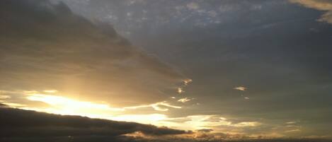 Un coucher de soleil sur la côte, avec des nuages au-dessus de l’eau.