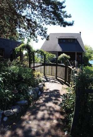 A pathway leading to a wooden gazebo with a dark roof, surrounded by lush greenery and a stone wall. - No cleaning fee. Close to downtown via direct bus. Private & beautiful view. (Seattle)
