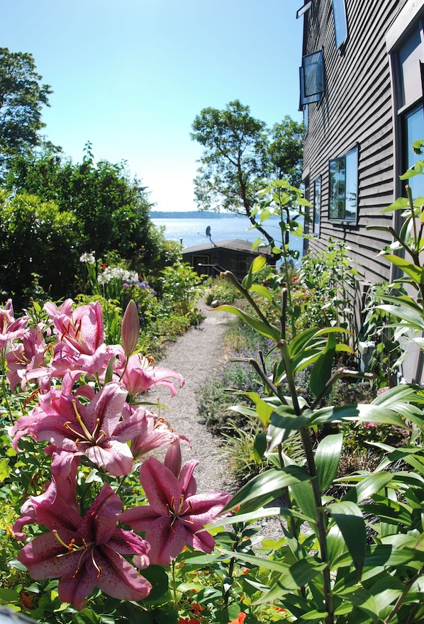 A garden with pink lilies and a pathway leading to a building with a view of the sea. - No cleaning fee. Close to downtown via direct bus. Private & beautiful view. (Seattle)
