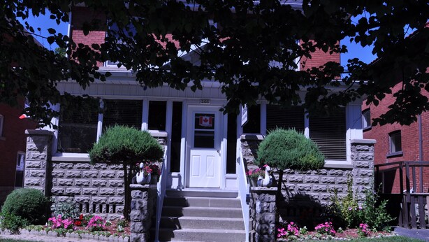 A two-story stone building with a white front door, a small porch, and a Canadian flag. - Ambassador B & B Guest Home (Stratford)
