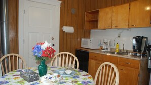 A kitchen with wooden cabinets, a microwave, a coffee maker, and a dining table with chairs. - Ambassador B & B Guest Home (Stratford)