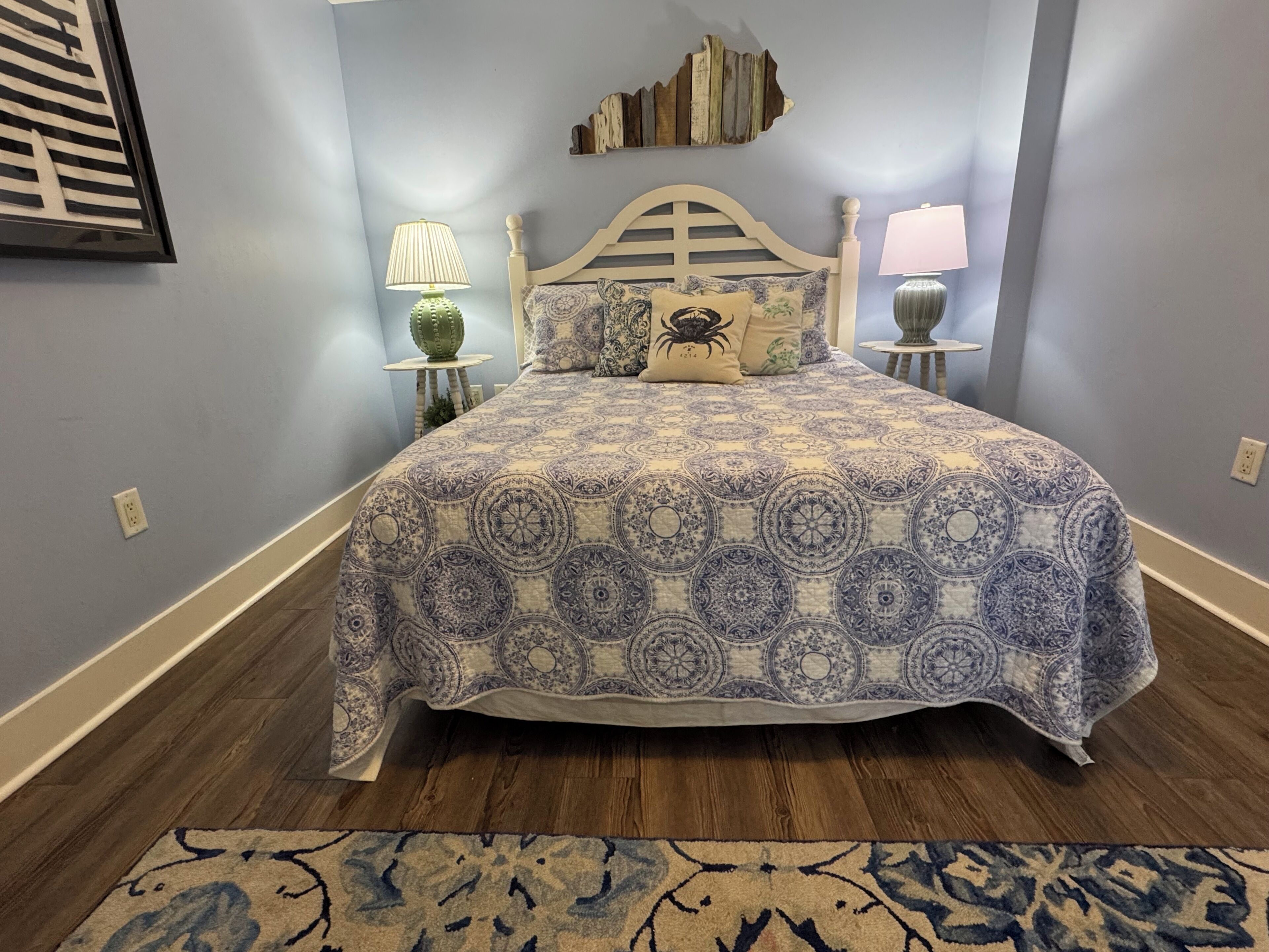 A bedroom with a bed, two bedside tables, a nightstand, a wall-mounted shelf, and a patterned rug.
