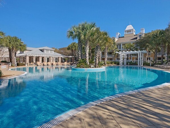 A large, clear swimming pool with a curved edge, surrounded by palm trees and a building with a dome roof.