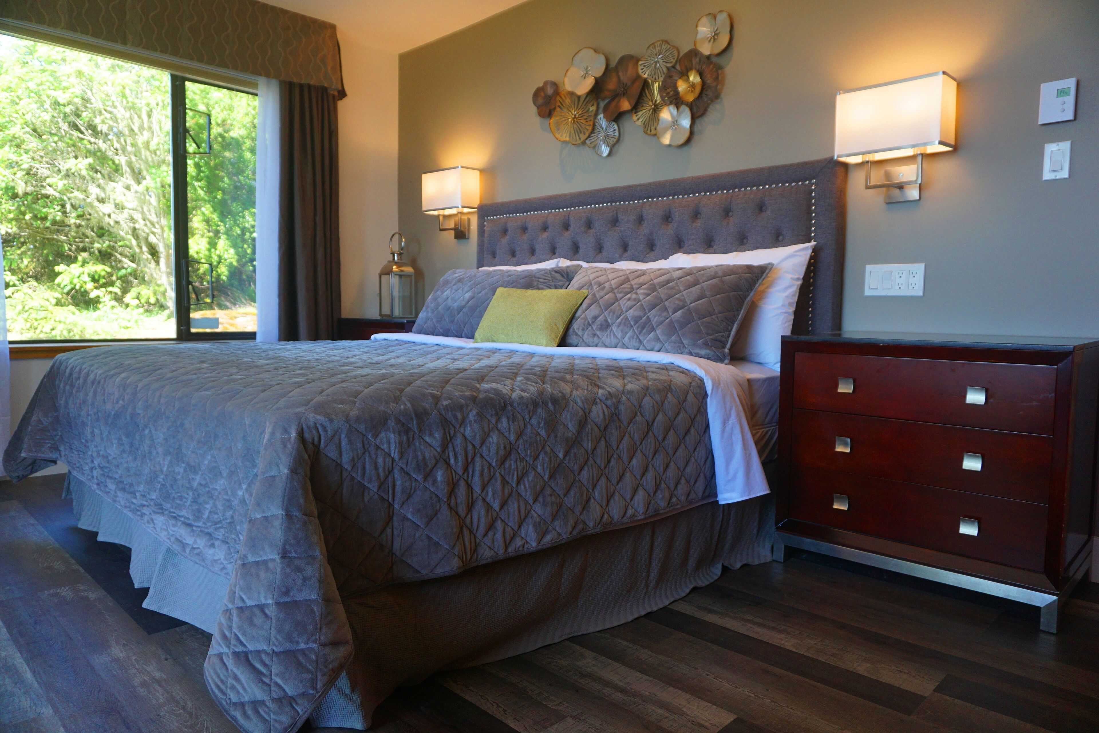 A bedroom with a large bed, a dresser, wall sconces, and a decorative wall piece.