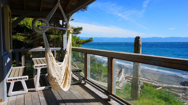 A wooden deck with a hammock, picnic table, and a view of the ocean and mountains.