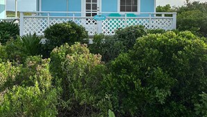A two-story house with a light blue exterior and white trim, featuring a covered porch with a white lattice railing. -  Starfish Beach Cottage (exuma)