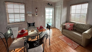 A cozy living room with a glass dining table, two chairs, a sofa, and a wooden ceiling. -  Starfish Beach Cottage (exuma)