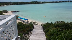 A wooden staircase leading to a beach with clear turquoise water, a sandy shore, and blue umbrellas. -  Starfish Beach Cottage (exuma)