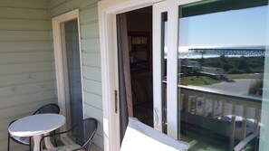 A balcony with a table and chairs, a sliding glass door, and a view of a bridge and water.