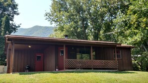 A wooden cabin with a red door, a covered porch, and a view of a mountain in the background.