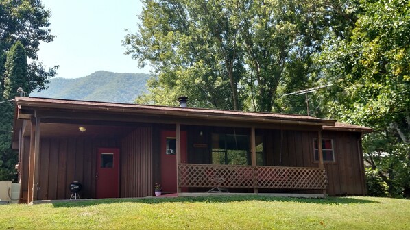 A wooden cabin with a red door, a covered porch, and a view of a mountain in the background.