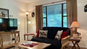A living room with a TV, a sofa, a coffee table, and a lamp.