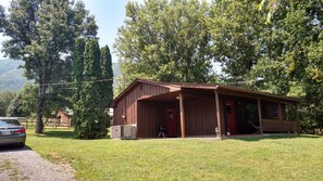 A wooden cabin with a porch, surrounded by trees and a gravel path.