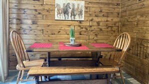 A wooden dining table with a red placemat, two wooden chairs, and a small plant centerpiece.