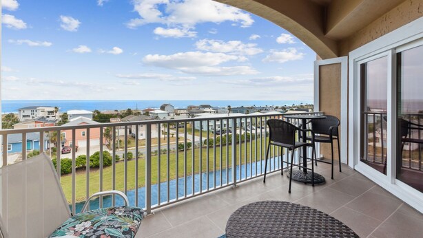 Ein Balkon mit Blick auf den Ozean, ein Pool und eine Essgegend mit Stühlen und einem Tisch.