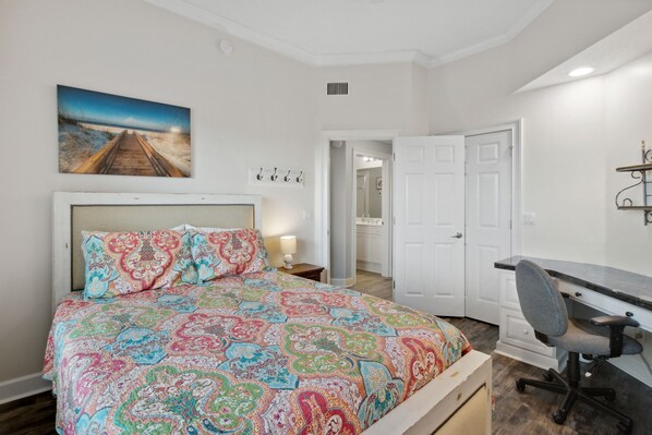 A bedroom with a bed, a desk, and a chair. There is a painting on the wall and a door leading to another room. - Stunning Ocean Views | Ocean Park Penthouse | Garage Access | Close to Beach (Fernandina Beach)