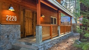 Une cabane en bois, construite sur des fondations en pierre, portant le numéro 2220, et dotée d’une véranda avec une balustrade en bois et des marches en pierre.