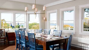Une salle à manger avec une table en bois dressée pour six personnes, des chaises bleues et de grandes fenêtres donnant sur l’extérieur.