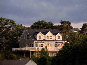 A two-story house with a gabled roof, a covered front porch, and a dock extending into a body of water.