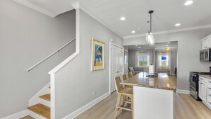 A kitchen with a central island, wooden staircase, and recessed ceiling lights. - Beautiful Town Home Beach Rental In Perdido Key Florida - Pool + Beach Access (Perdido Key)