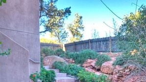 Un sendero de concreto con escalones que conducen a una casa, rodeado de follaje y rocas.