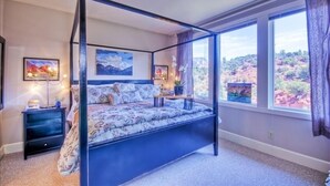 Una cama con dosel con un edredón floral, dos mesitas de noche con lámparas y obras de arte en las paredes.