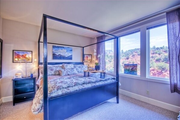 A four-poster bed with a floral bedspread, two bedside tables with lamps, and artwork on the walls.