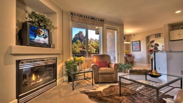Una sala de estar con chimenea, televisor, sillón de cuero, mesa de centro de vidrio y vista a un paisaje montañoso a través de un ventanal grande.
