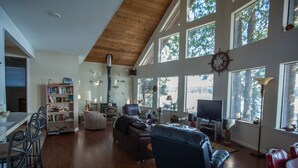 A spacious living room with a high ceiling, large windows, a fireplace, a television, and a bookshelf. - Waterfront Getaway, Beautiful Hood Canal (Brinnon Wa)