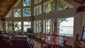 A spacious living room with a large window overlooking a body of water, a cozy seating area, and a dining table. - Waterfront Getaway, Beautiful Hood Canal (Brinnon Wa)