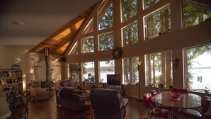 A spacious living room with a high ceiling, large windows, a fireplace, a dining area, and a bookshelf. - Waterfront Getaway, Beautiful Hood Canal (Brinnon Wa)
