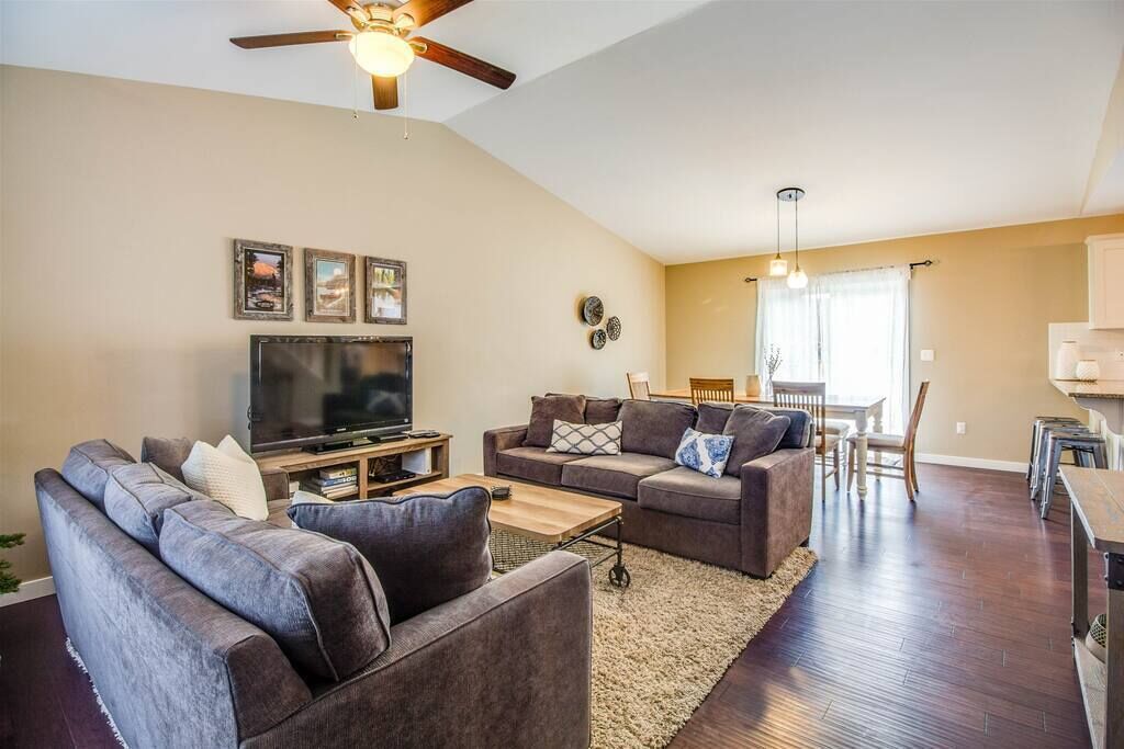 A living room with two sofas, a TV, and a ceiling fan. There is a dining area with a table and chairs.