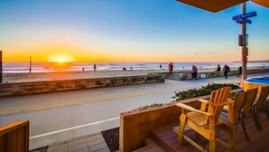 Vista al atardecer desde un patio frente a la playa, con sillas de madera y una señal de calle que dice "SAN RAFAEL".