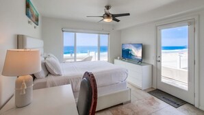 Habitación de hotel con cama, escritorio, silla, televisor y balcón con vista al océano.