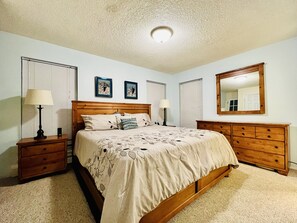 A bedroom with a wooden bed, two bedside tables, a dresser, and a ceiling light. - Ground floor, remodeled, 3 bedroom condo is 10 minutes to Winter Park Ski Resort (Winter Park)