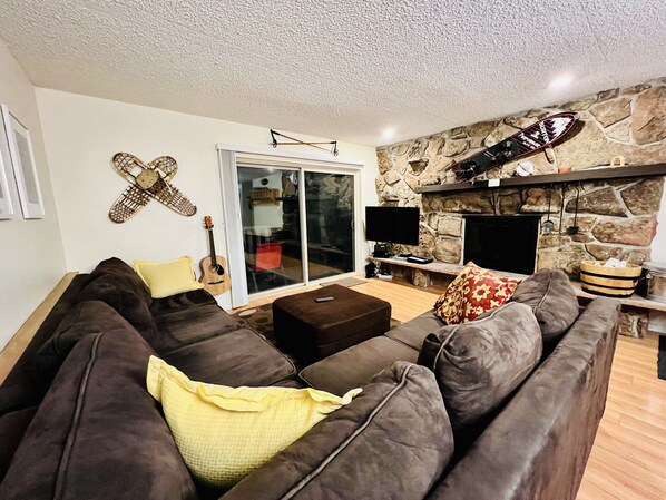 A living room with a brown leather sofa, a yellow pillow, a guitar, a flat-screen TV, and a stone fireplace. - Ground floor, remodeled, 3 bedroom condo is 10 minutes to Winter Park Ski Resort (Winter Park)