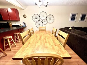 A dining area with a wooden table, six chairs, a red kitchen area, and a black sofa. - Ground floor, remodeled, 3 bedroom condo is 10 minutes to Winter Park Ski Resort (Winter Park)