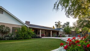 A modern house with a covered patio, a well-maintained lawn, and a variety of plants and flowers. - Hidden, Lush Treasure Close to Everything...Your Own Private Resort! (Mesa)