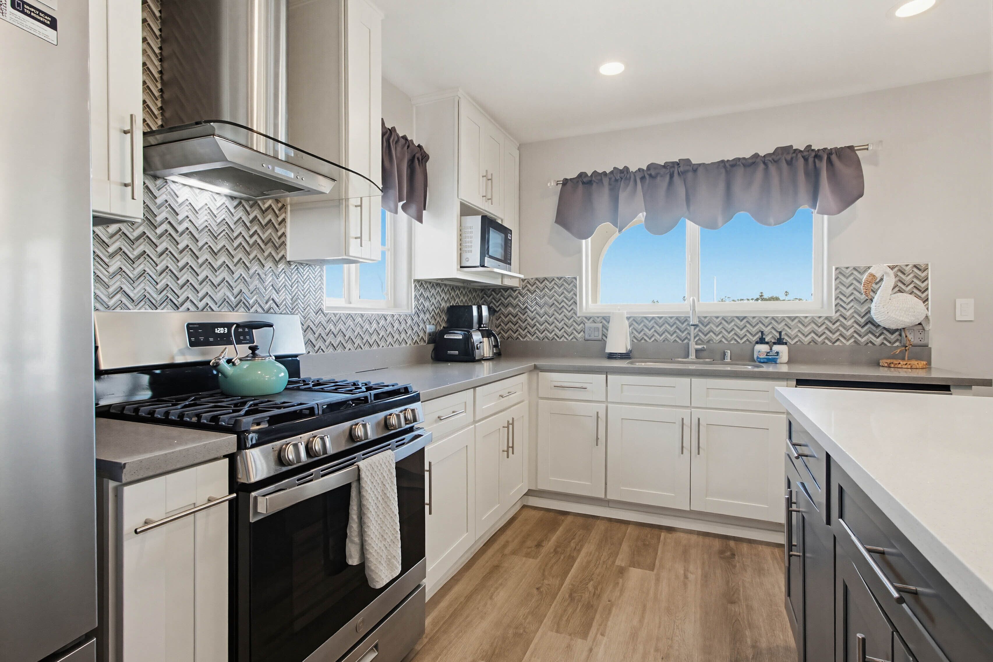 Una cocina moderna con armarios blancos, estufa, microondas y una ventana con cortinas.