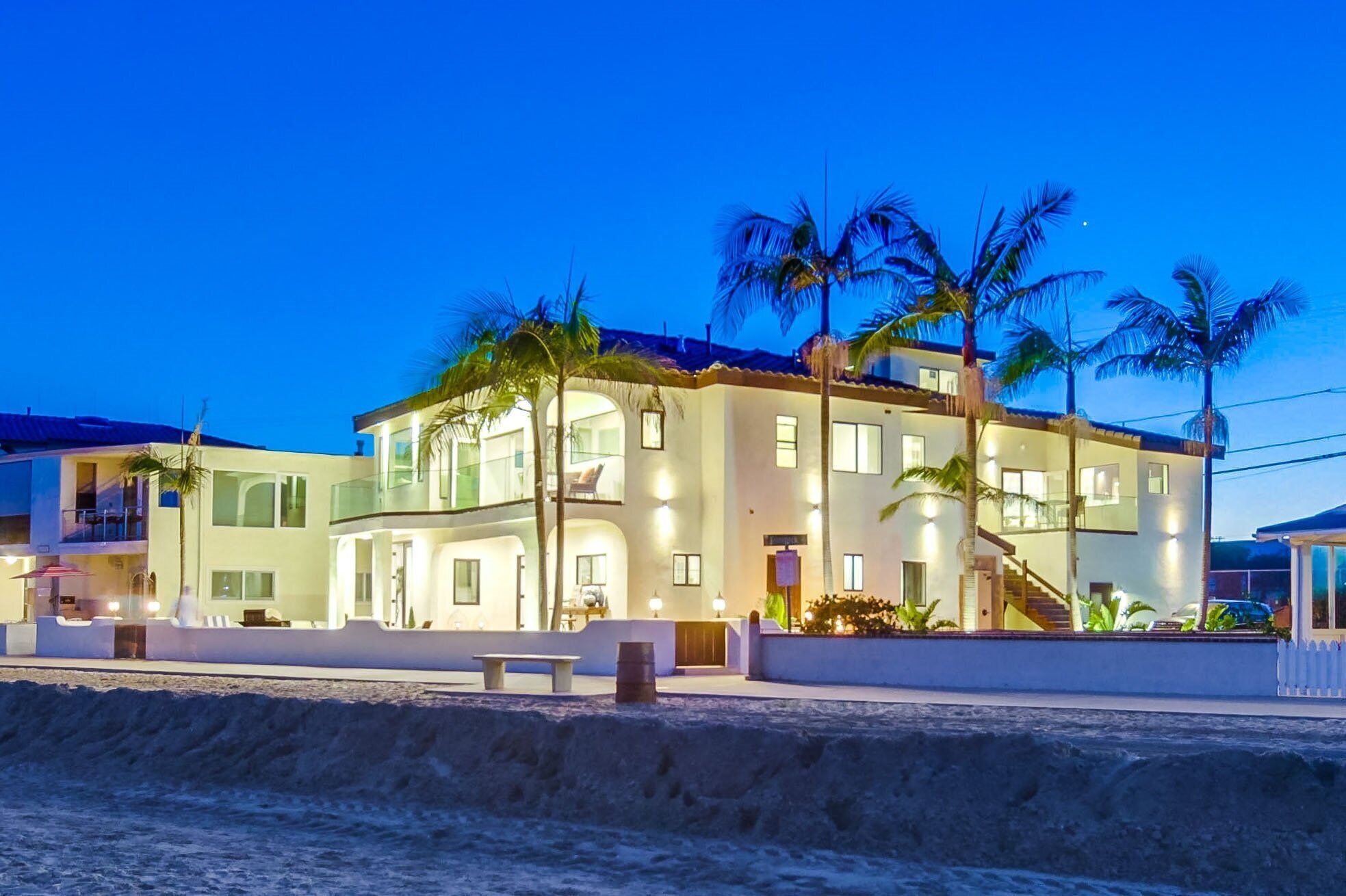 Ein mehrstöckiges Strandhotel mit Balkonen, Palmen und einem Sandstrand im Vordergrund.