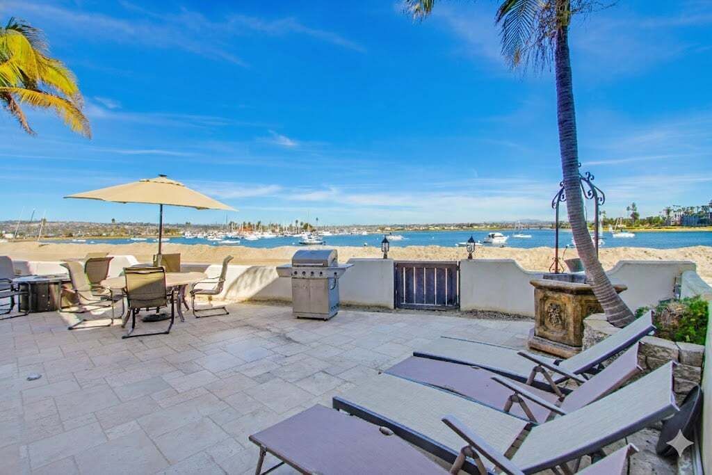 Eine Terrasse mit Liegestühlen, einem Grill und Blick auf Strand und Meer.