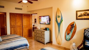 A bedroom with two beds, a dresser, a TV, and surfboards on the wall. - Las Mañanitas LM E3402 (Los Cabos)