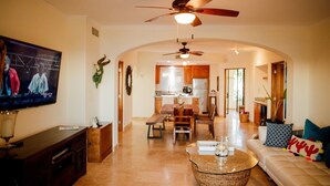 A spacious living room with a television, a ceiling fan, a dining area, and a kitchen in the background. - Las Mañanitas LM E3402 (Los Cabos)