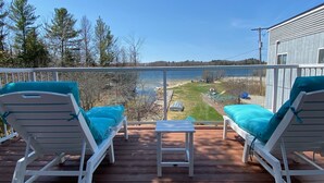Une terrasse en bois avec deux chaises longues blanches et une petite table, donnant sur un lac et une zone herbeuse.