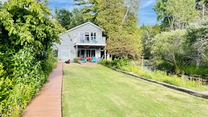 Une maison à deux étages avec un patio couvert, une pelouse et un petit étang.