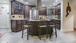 A modern kitchen with dark wood cabinets, a stainless steel range hood, and a central island with bar stools. - Top Floor. Top Views. Top of Whistler. 
The Penthouse at the Carleton Lodge. (Whistler)