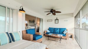 A spacious balcony with wicker furniture, a ceiling fan, and a view of the outdoors. - Relax on the oversized lanai featuring an outdoor kitchen and mid-water view. (Naples)
