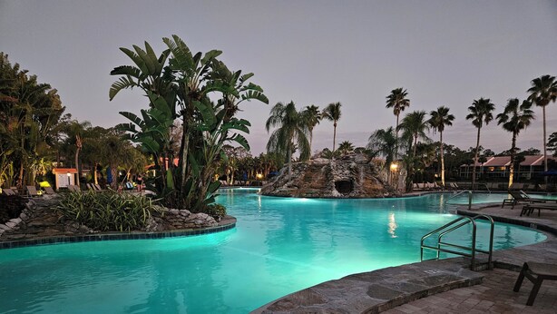 A swimming pool with a natural rock feature, surrounded by palm trees and lounge chairs. - Relax on the oversized lanai featuring an outdoor kitchen and mid-water view. (Naples)